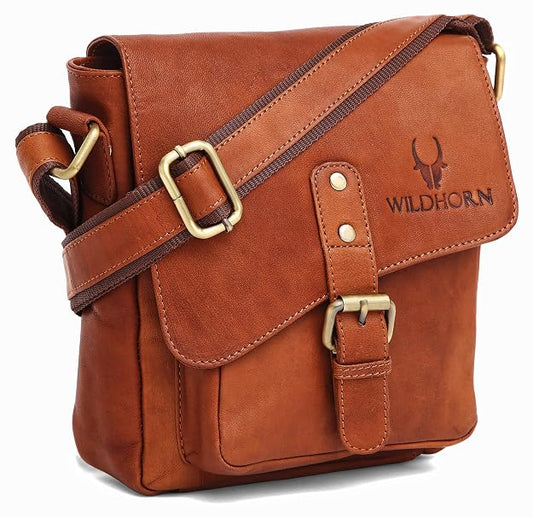 A brown leather messenger bag with a flap front, adjustable shoulder strap, and brass-tone hardware. The brand name 'WILDHORN' with a horn logo is embossed on the front flap.