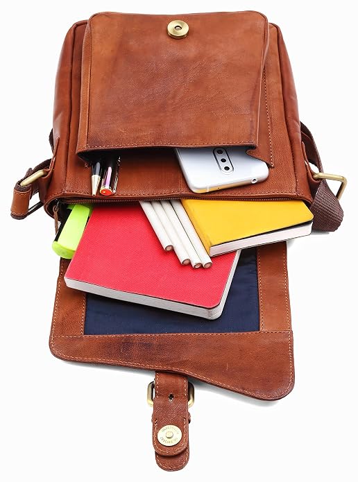 A brown leather messenger bag shown open, filled with notebooks, pens, a smartphone, and a yellow folder, photographed on a plain white background.