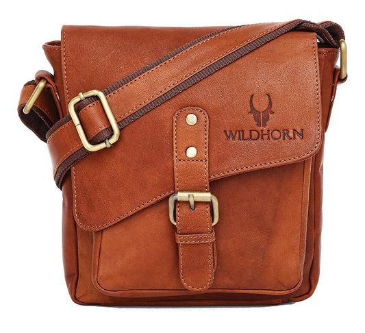 A brown leather crossbody bag with brass hardware, featuring a front flap with a buckle strap and the brand name 'WILDHORN' embossed on the side, set against a plain white background.