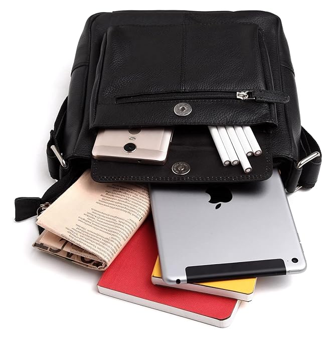 A black leather messenger bag shown open with its front pocket expanded to reveal storage space, filled with a smartphone, notebooks, pens, and a tablet on a white background.