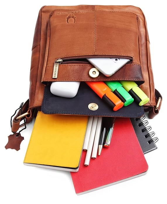 A brown leather messenger bag shown open on a white background, with its front pocket and flap compartments filled with a smartphone, earbud case, highlighters, pens, sticky notes, and notebooks.