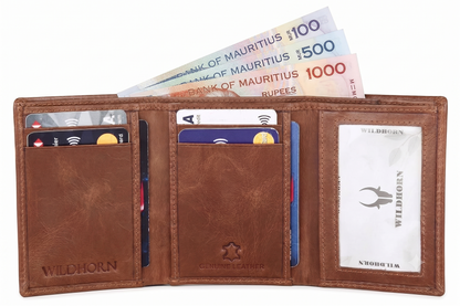 A brown leather bifold wallet shown open on a white background, containing credit cards, cash, and a printed ID card. The wallet has 'WILDHORN' branding embossed on the lower left and center, and a clear ID window on the right. Available in Mauritius.