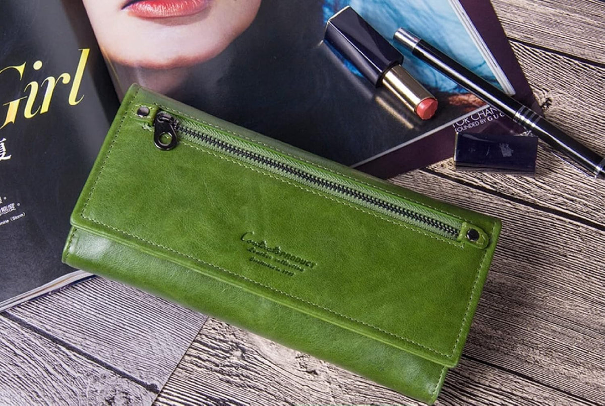 A green leather long wallet with a top zipper, displayed on a rustic wooden surface next to a magazine and cosmetics shop in Mauritius at Bags.mu