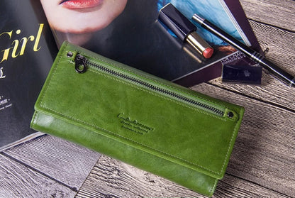 A green leather long wallet with a top zipper, displayed on a rustic wooden surface next to a magazine and cosmetics shop in Mauritius at Bags.mu