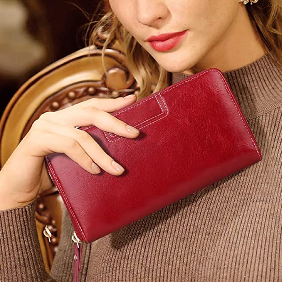 A woman in a brown ribbed sweater holds a deep red leather clutch wallet against a warm, blurred background available in Mauritius